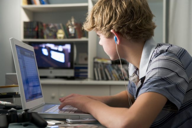 Young boy in bedroom using laptop and listening to MP3 player the Real Cost of Raising Kids